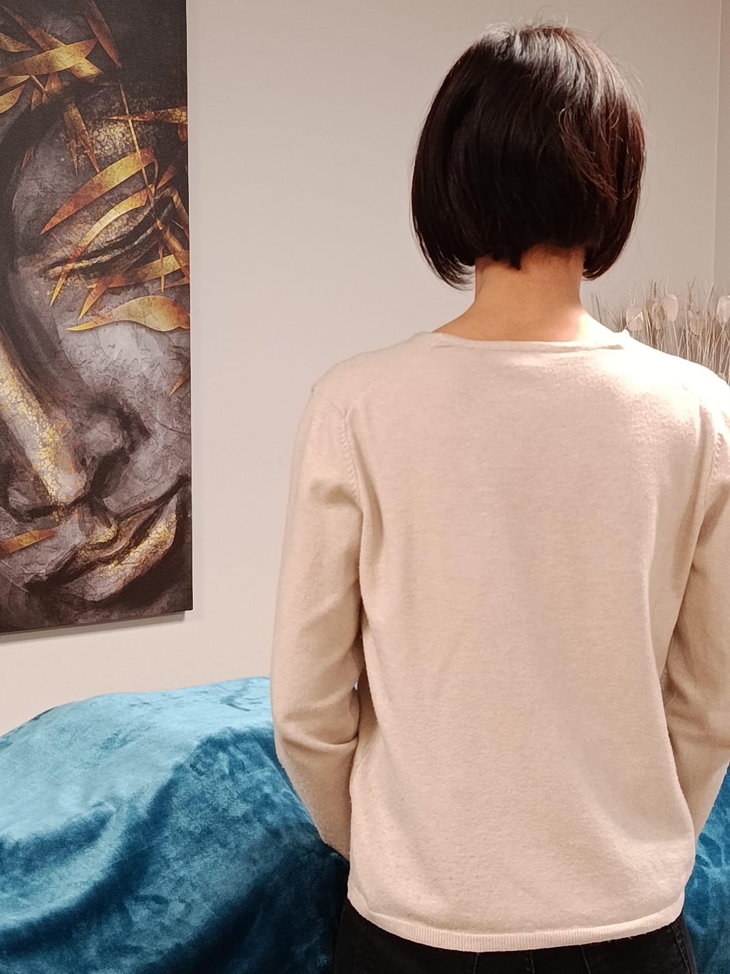 Praticienne de Reiki de dos, devant une table de soin recouverte d’un plaid, dans un espace calme et respecté.